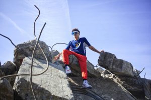 Young male model in vibrant attire sits on concrete rubble in a striking outdoor photoshoot.