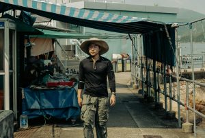 Man in casual wear walking by outdoor market stalls near a waterfront.
