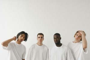 Four diverse young men posing in a minimalist studio setting with white background.